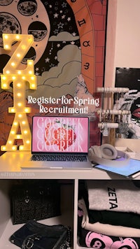 a desk with a laptop, t shirts, and a sign that says register for spring recruitment