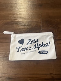 a white zipper pouch with the word zeta alpha on it